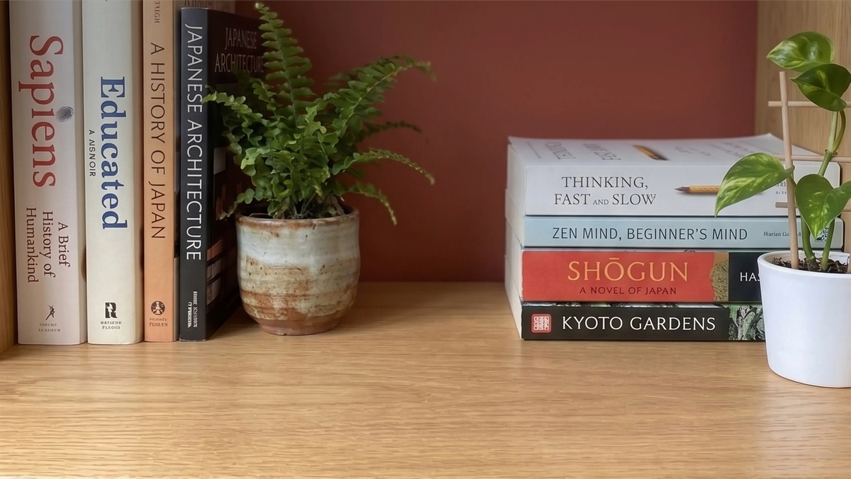 Warm wooden bookshelf with upright architecture and history books, a fern in a ceramic pot and a stack of books, the shelf setting used to display a mini mosque building blocks model